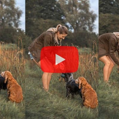 Video thumbnail: a woman with two dogs in a grassy field, bending to pet them; a red play button overlays the center.